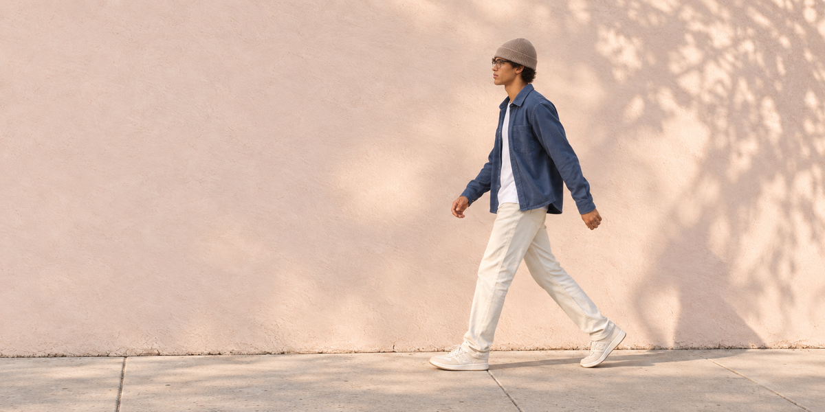 Miles wearing a natural cashmere beanie, walking beside a pink-beige wall in Cupertino sunlight