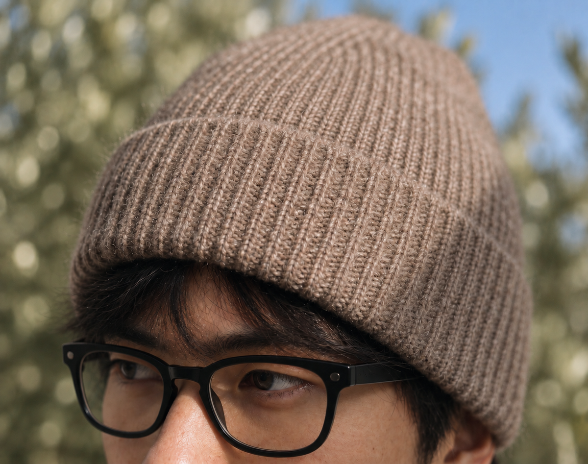 Evan wearing the FRUAA Natural cashmere beanie, close-up against softly blurred trees and blue sky