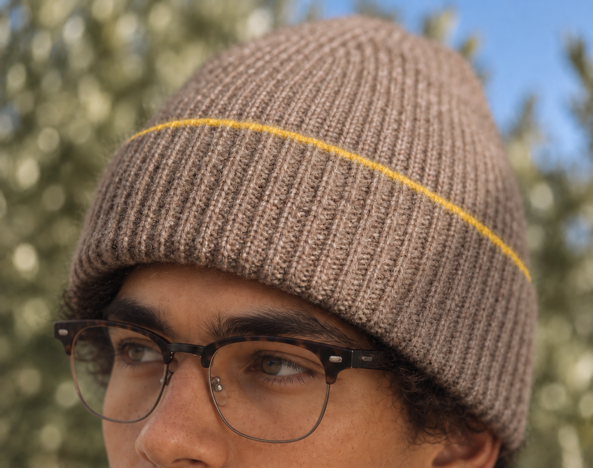 Miles wearing the FRUAA Yellow Line cashmere beanie, close-up against softly blurred trees and blue sky